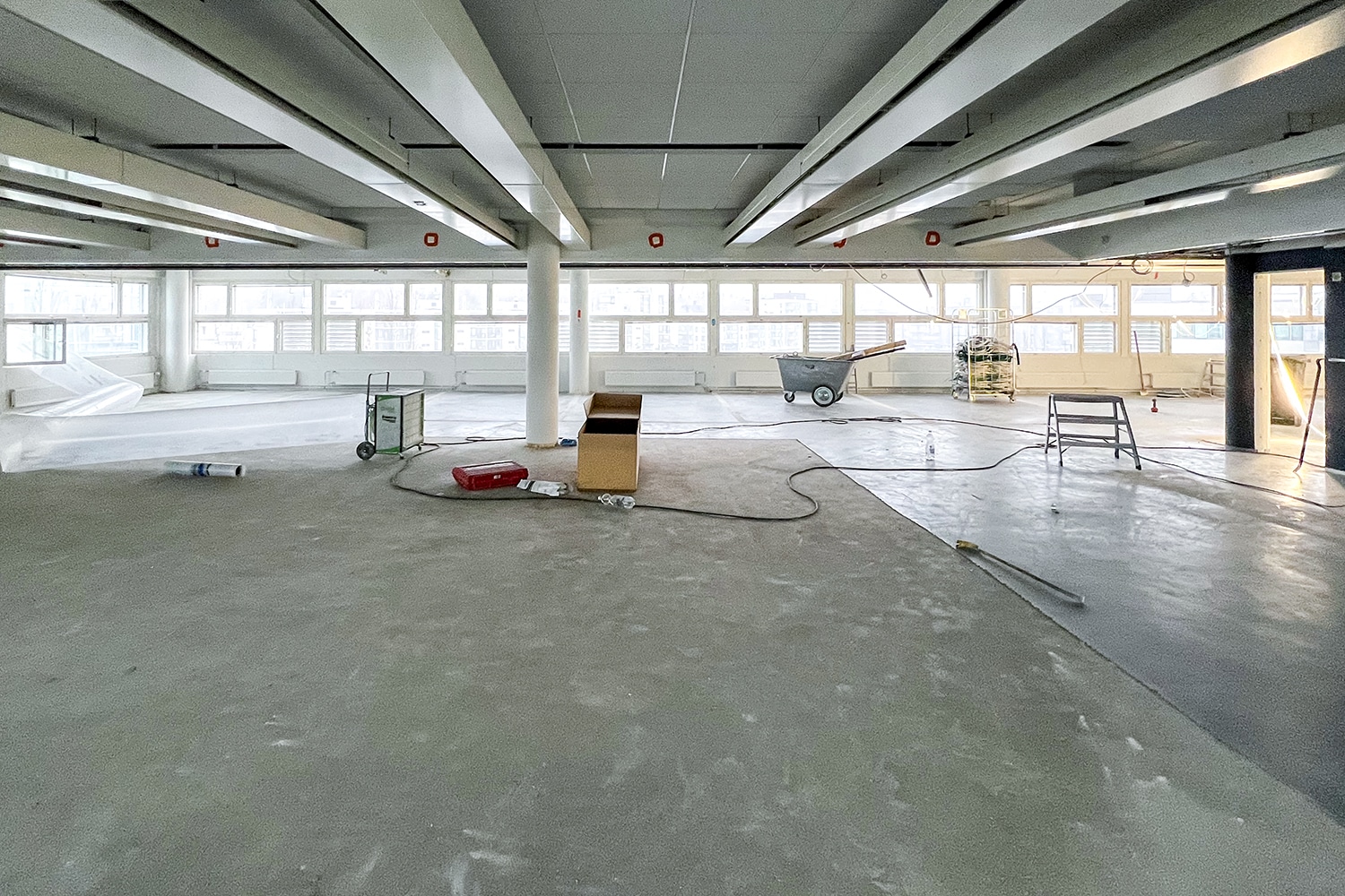 Suuri toimistotila purettuna betonille, lattialla muutamia työkaluja.