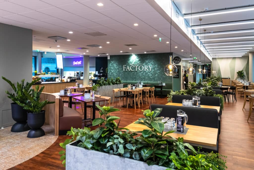 Factoryn ranintolasali, jossa on useita pöytäryhmiä ja huonekasveja.